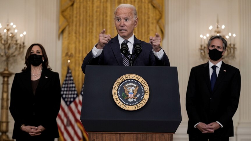 Biden gestures at the podium during his speech, flanked by Vice President Kamala Harris and Secretary of State Anthony Blinken