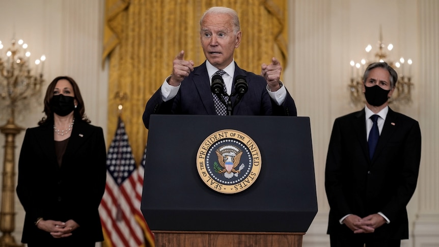 Biden gestures at the podium during his speech, flanked by Vice President Kamala Harris and Secretary of State Anthony Blinken