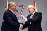 Boris Johnson and Scott Morrison smile and shake hands in front of a G7 sign.