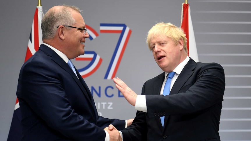 Boris Johnson and Scott Morrison smile and shake hands in front of a G7 sign.