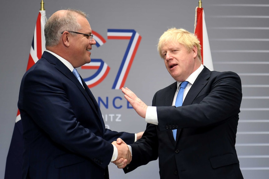 Boris Johnson and Scott Morrison smile and shake hands in front of a G7 sign.