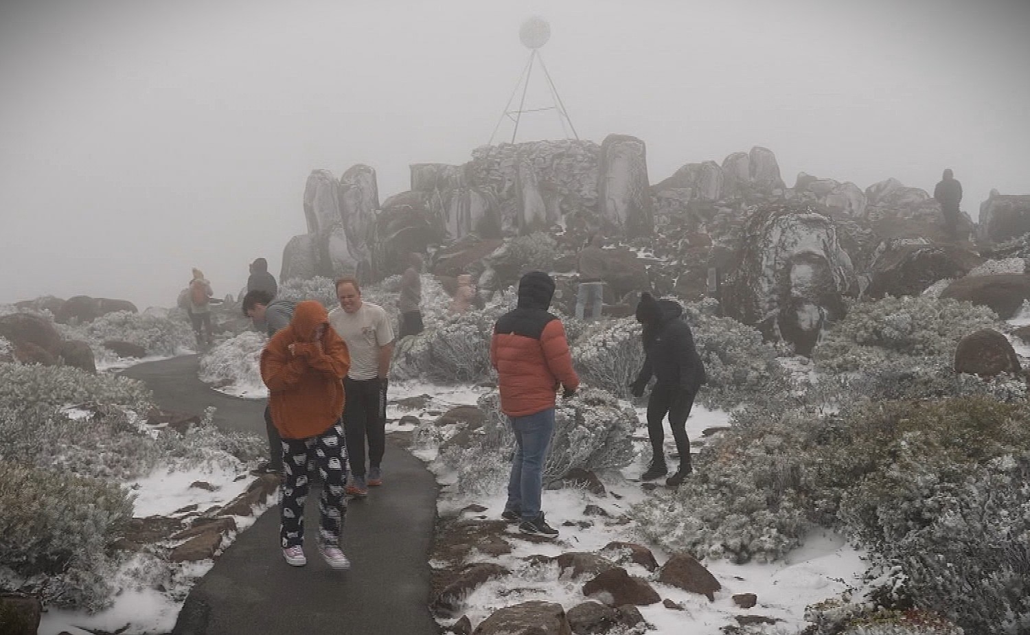Tourists exploring the snowy conditions on summit of mountain.