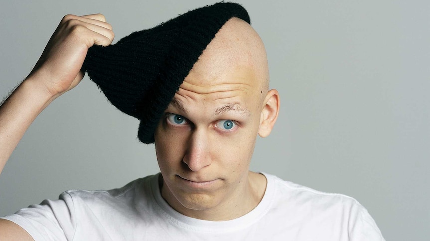 A man with a bald head removes a black beanie.