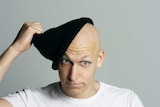 A man with a bald head removes a black beanie.