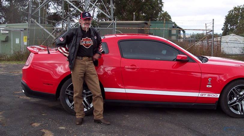 An elderly man standing beside a red car