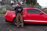An elderly man standing beside a red car