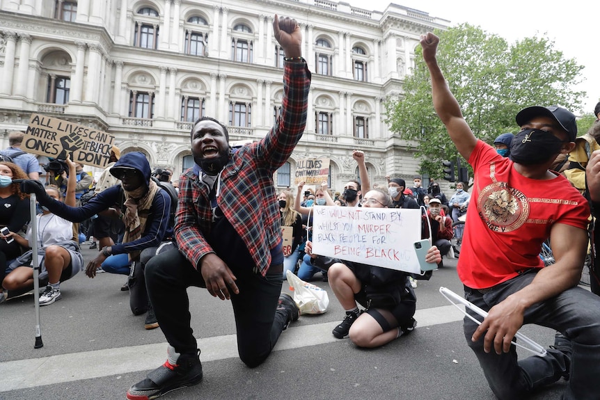 Protesters kneel down in the street while shouting and holding on fist in the air.