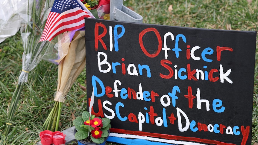 A poster painted with red white and blue reads RIP Officer Brian Sicknick defender of the US Capitol and Democracy