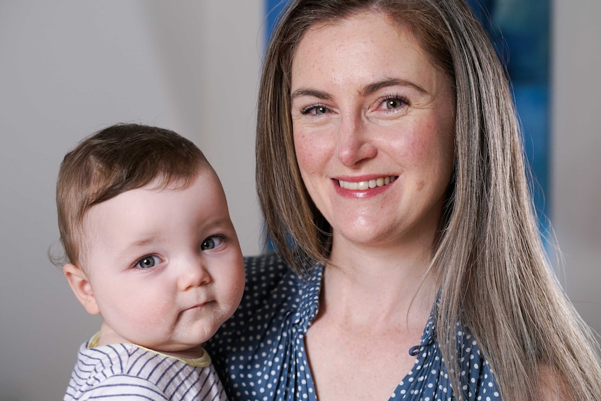 A woman holding her baby smiling at the camera.