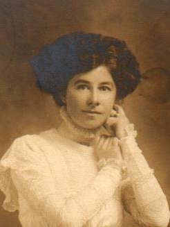 A black and white photo of a woman with brown hair, wearing a white lacy dress.