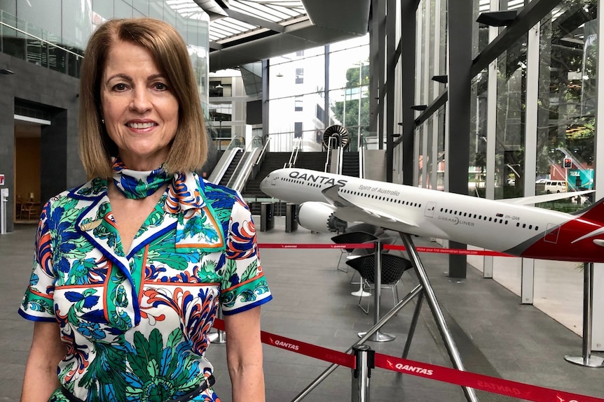 A woman wearing a Qantas host uniform stands in front of a model plane.