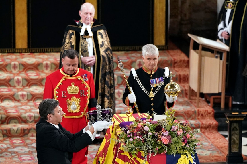 A man is pictured holding the Queen's crown, another man the scepter and orb as they lift it off the coffin.