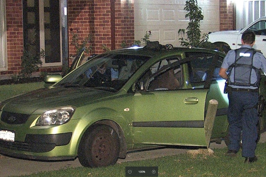 Police check a green sedan that has come to rest between wooden bollards in a cul-de-sac.