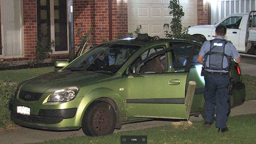 Police check a green sedan that has come to rest between wooden bollards in a cul-de-sac.