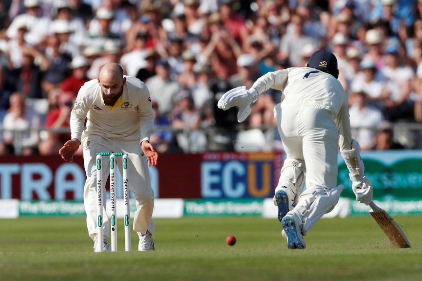 Australia bowler Nathan Lyon stands over the stumps without the ball while England batsman Jack Leach completes a run.