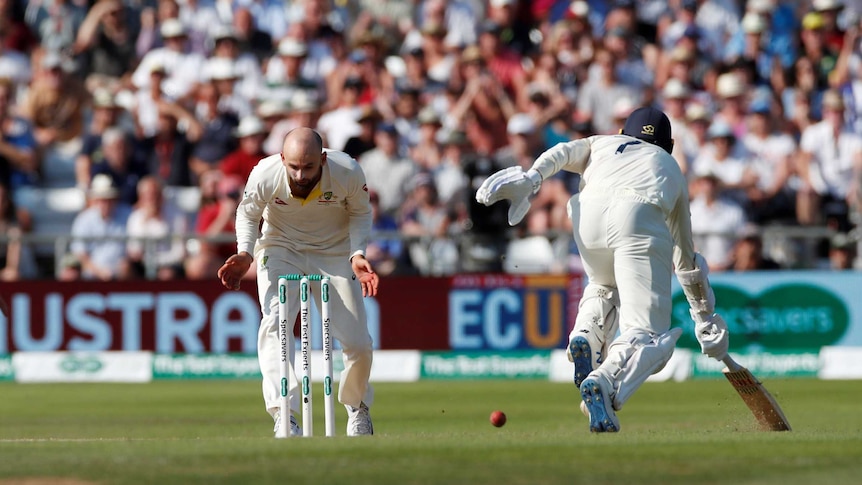 Australia bowler Nathan Lyon stands over the stumps without the ball while England batsman Jack Leach completes a run.