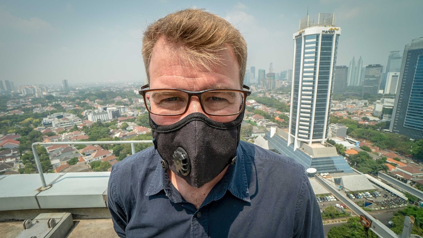 David Lipson stands on a balcony wearing a black face mask