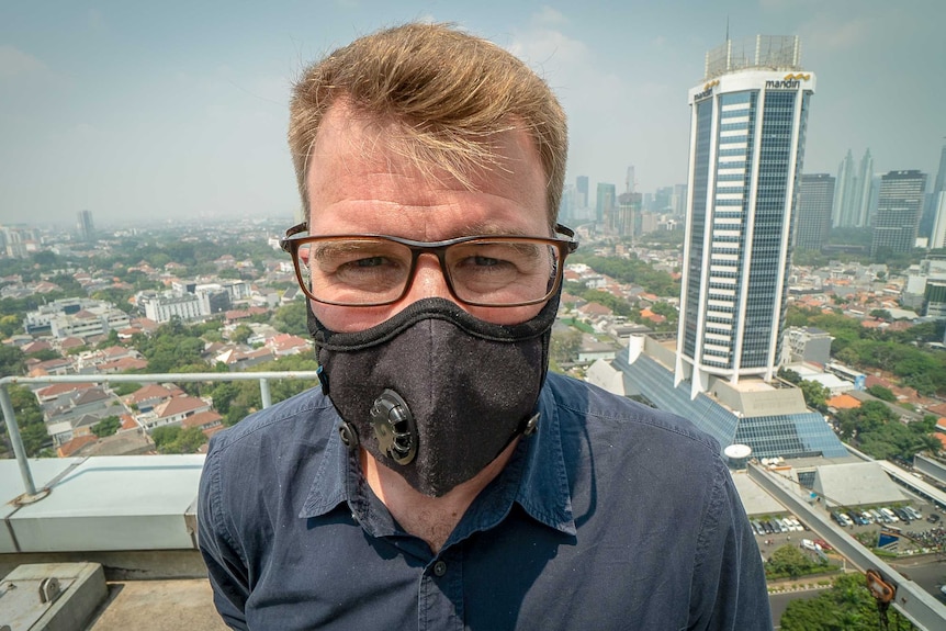 David Lipson stands on a balcony wearing a black face mask