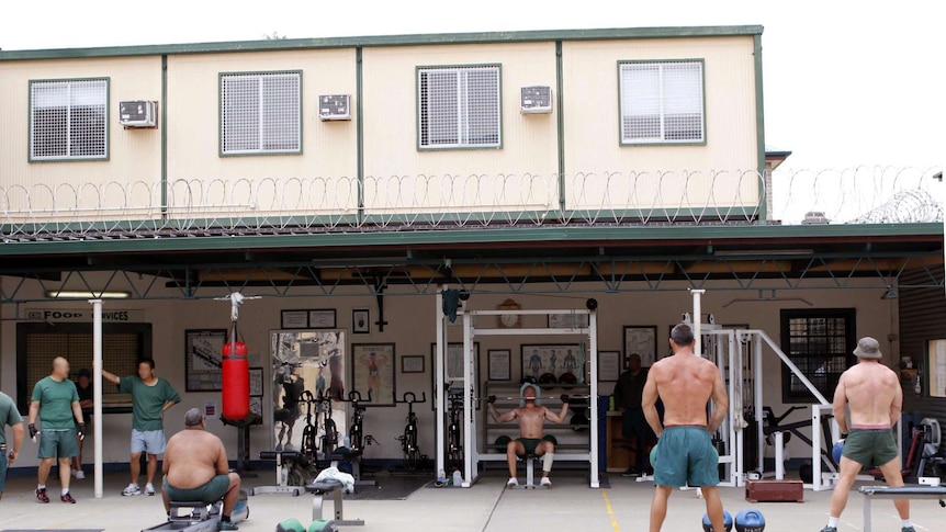 Five men with big muscles use gym equipment in the courtyard of the jail.