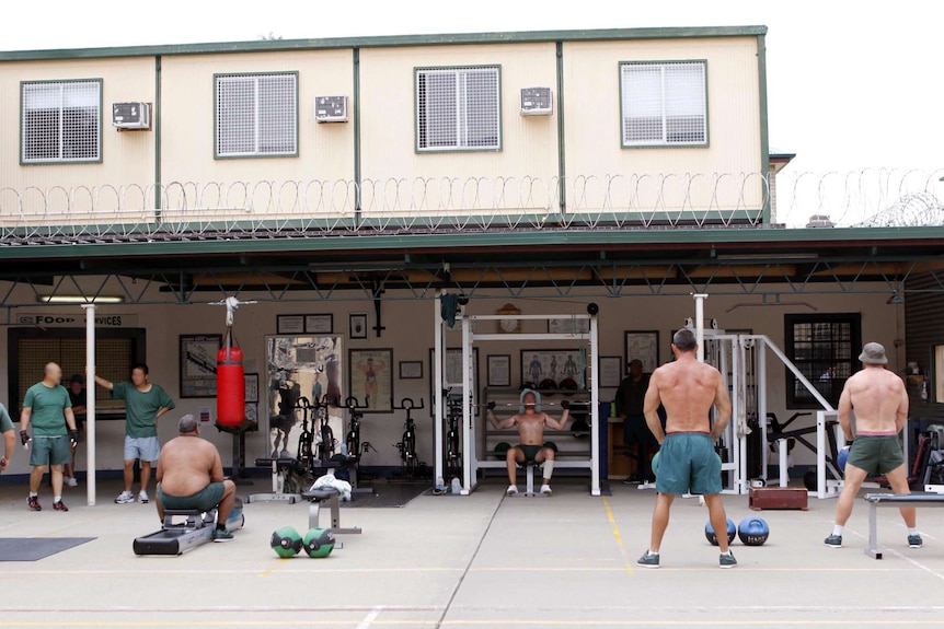 Five men with big muscles use gym equipment in the courtyard of the jail.