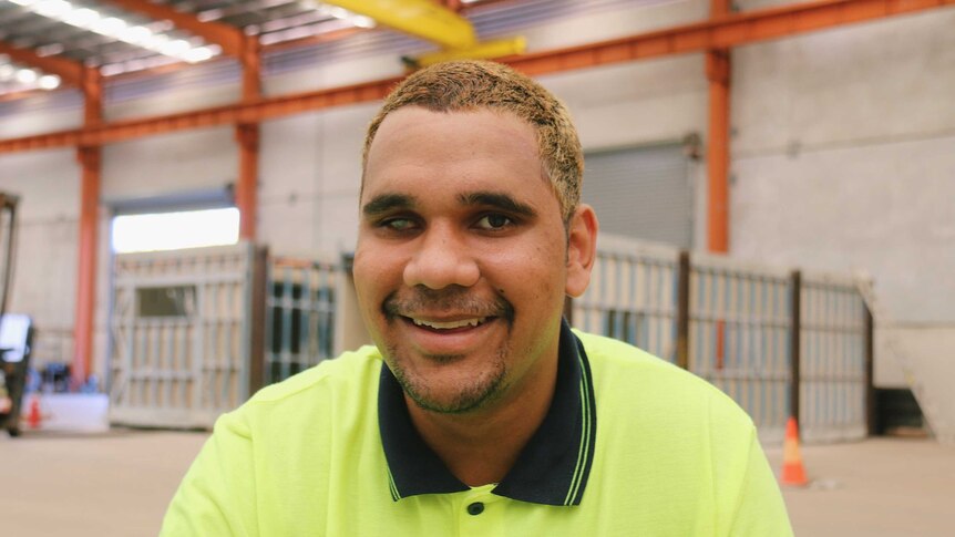 Trent wearing a fluorescent work shirt, he is smiling and has short, bleached blonde hair.