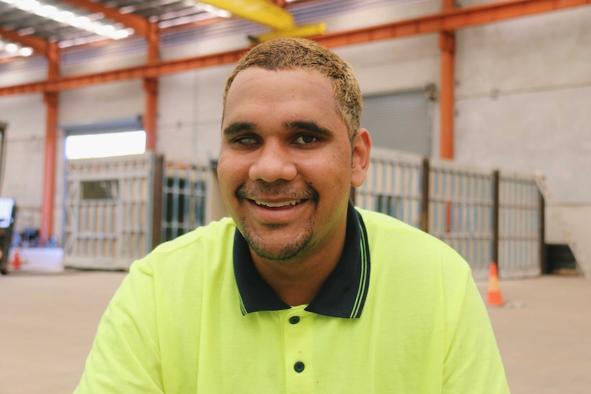 Trent wearing a fluorescent work shirt, he is smiling and has short, bleached blonde hair.