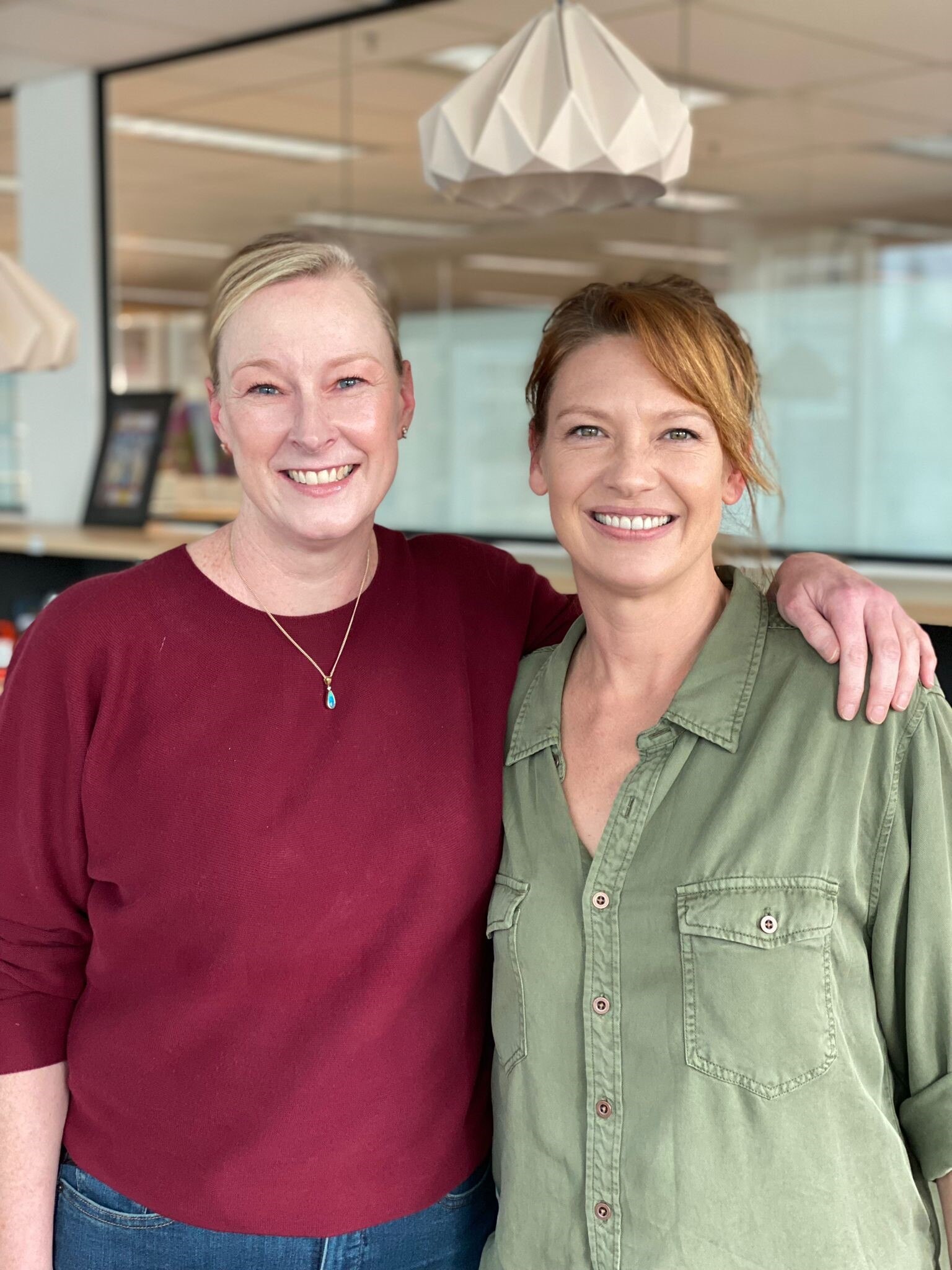 Two women with arms around each other smiling at camera.
