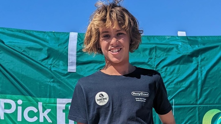 A young surfer smiles at the camera.