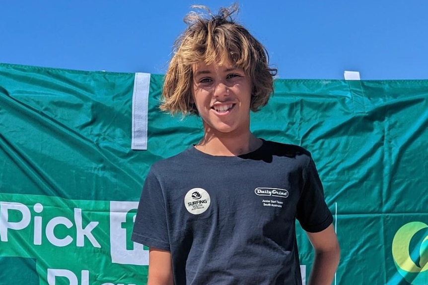 A young surfer smiles at the camera.