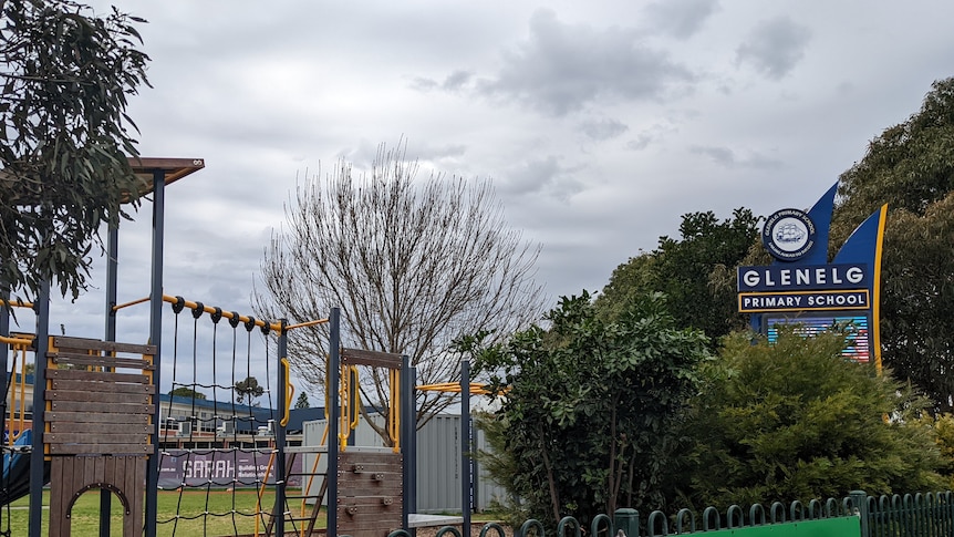 play equipment and sign of a school with greenery inside a fence that has print ads on it