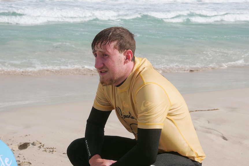 A man crouching near the ocean in a wetsuit. 