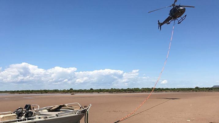 A helicopter flies above a boat which it has connected by rope to.