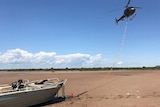 A helicopter flies above a boat which it has connected by rope to.