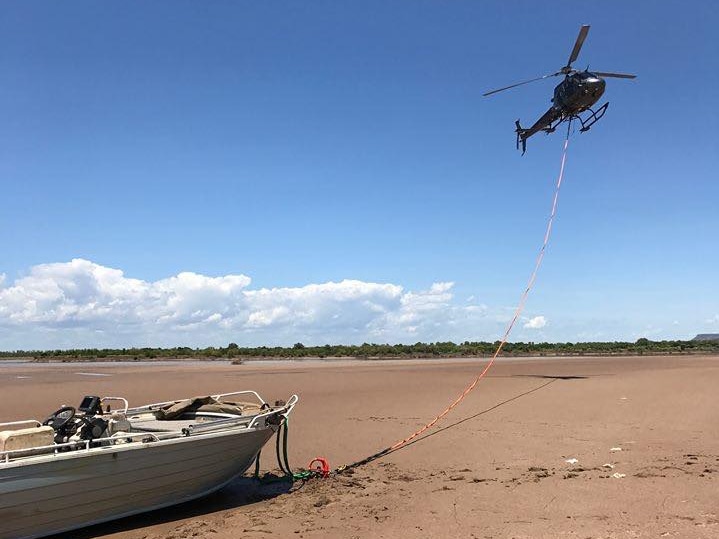 A helicopter flies above a boat which it has connected by rope to.