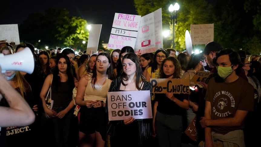 Young women holding signs at a night time protest