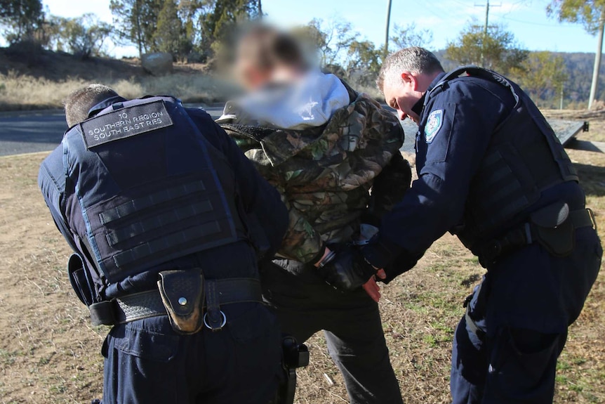 Two law enforcement officers handcuff a suspect of illegal narcotic activities.