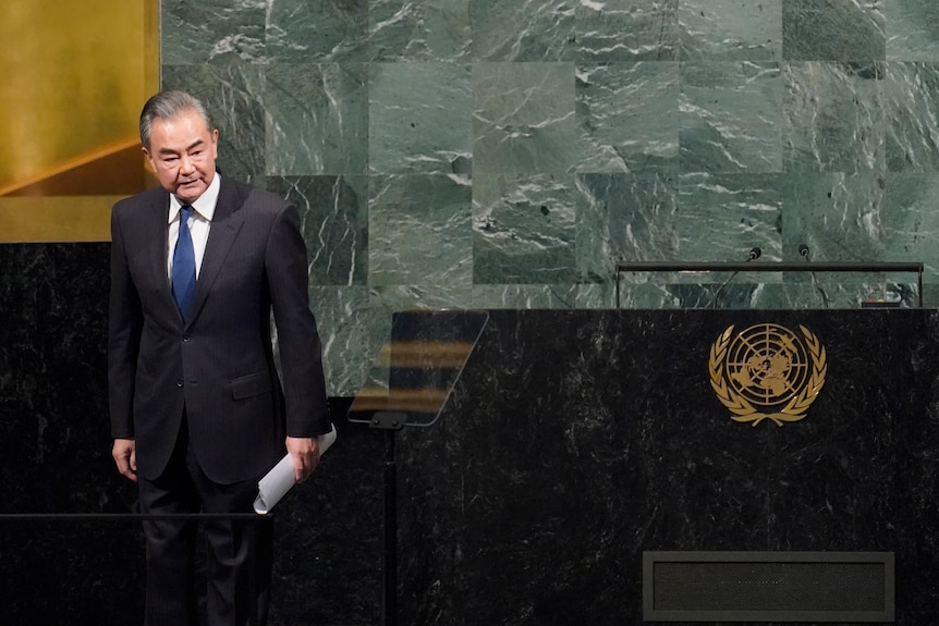 A man in a suit looks to the right while holding a sheet of paper in the UN General Assmebly hall