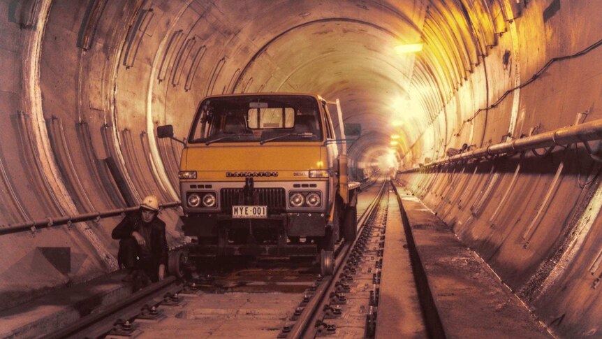 A yellow truck with guides to keep it on train tracks in a rail tunnel