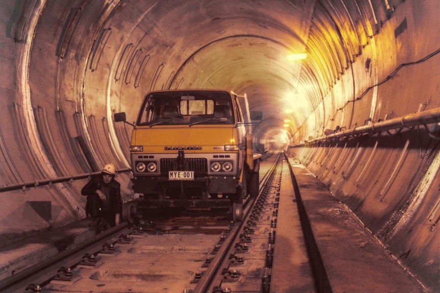A yellow truck with guides to keep it on train tracks in a rail tunnel