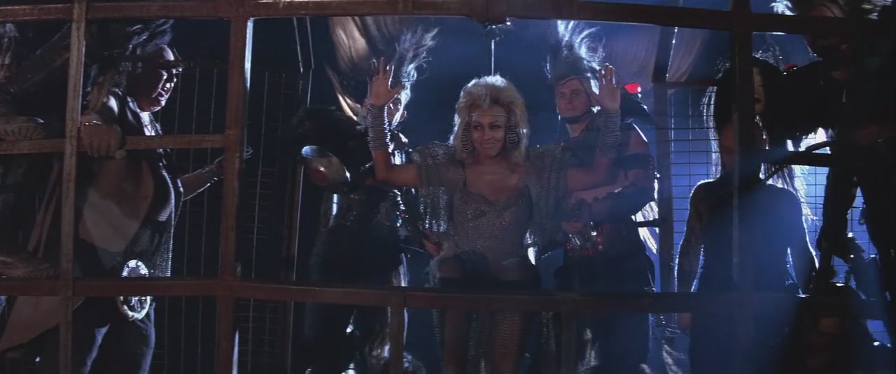 A scene from a movie showing a post-apocalyptic scene with men and a woman in costume.