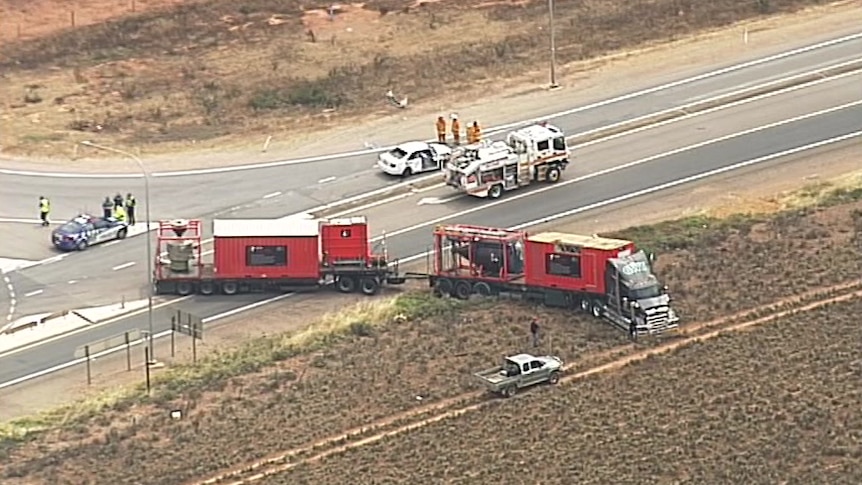 A truck parked half on and off the road and a white sedan on a highway surrounded by emergency service vehicles