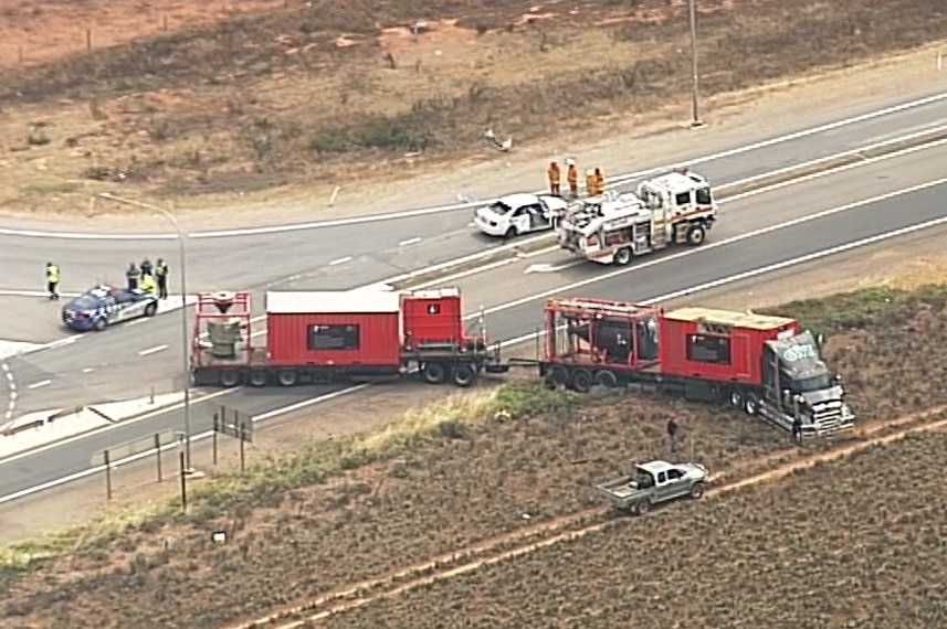 A truck parked half on and off the road and a white sedan on a highway surrounded by emergency service vehicles