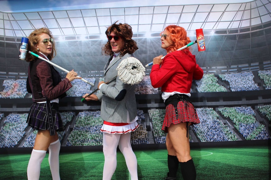 Lisa, Andrew and Car wear blazers and short tartan skirts holding broom sticks as croquet mallets.