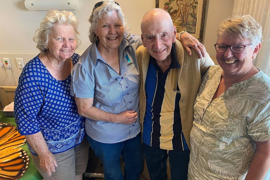 three women embrace a man smiling at the camera