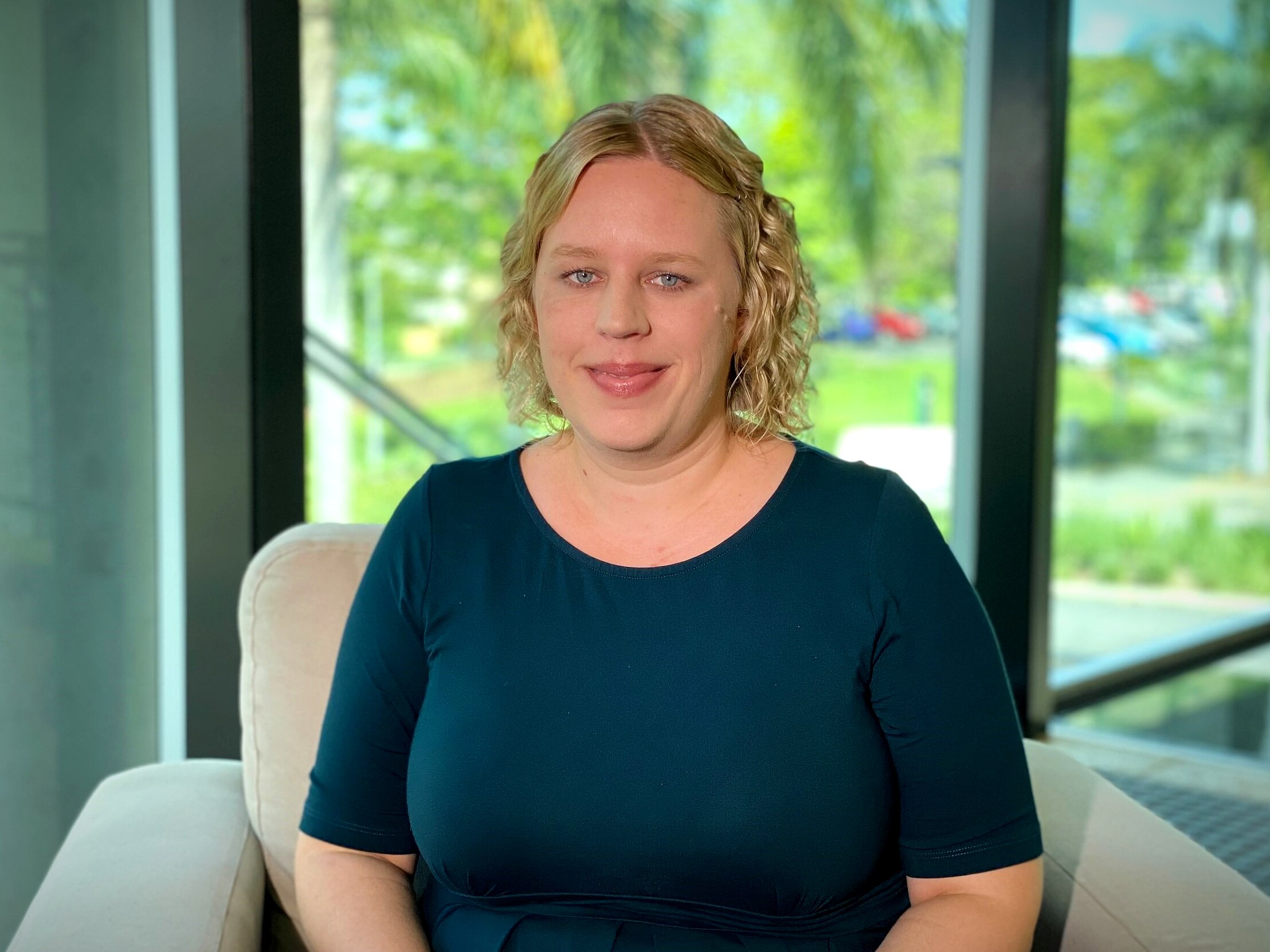 A woman sits in an armchair in front of window.