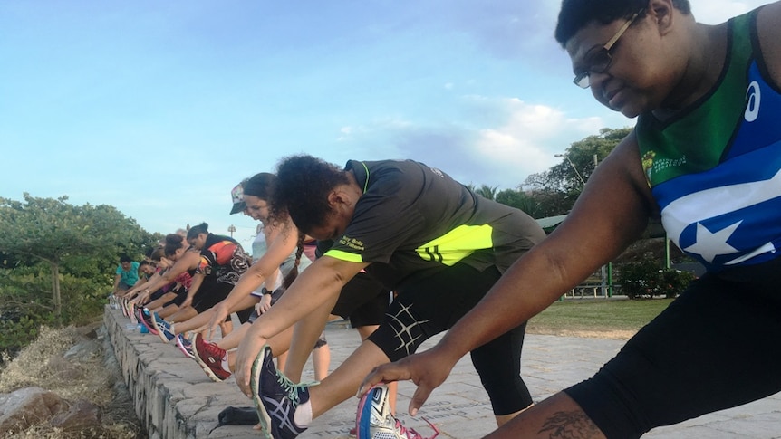 About a dozen runners reaching forward to their toe to stretch their hamstring muscles after a run