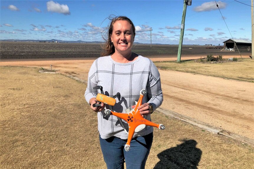 A woman stands holding a drone in a paddock