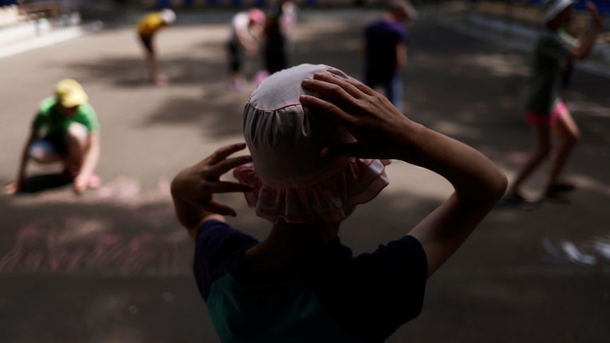 Child holds hat watching other children play