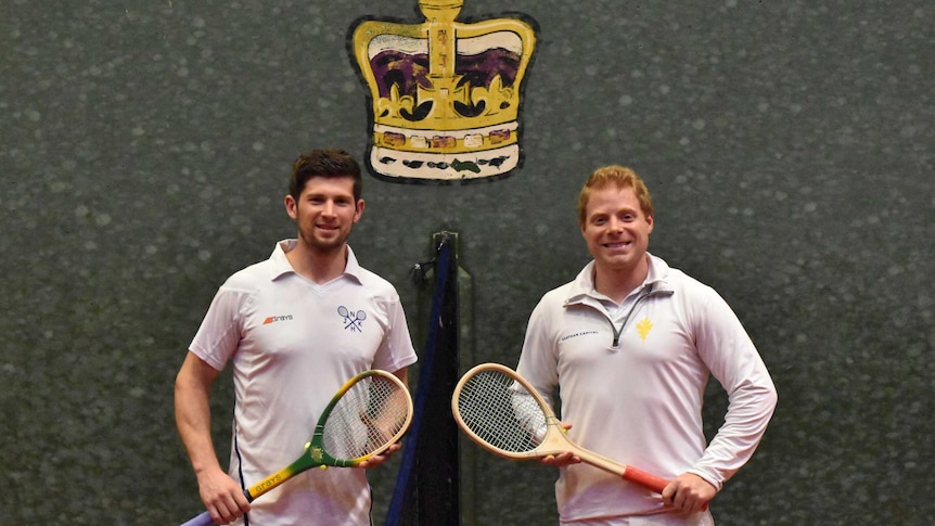 Two players with wooden racquets pose in front of a painted crown