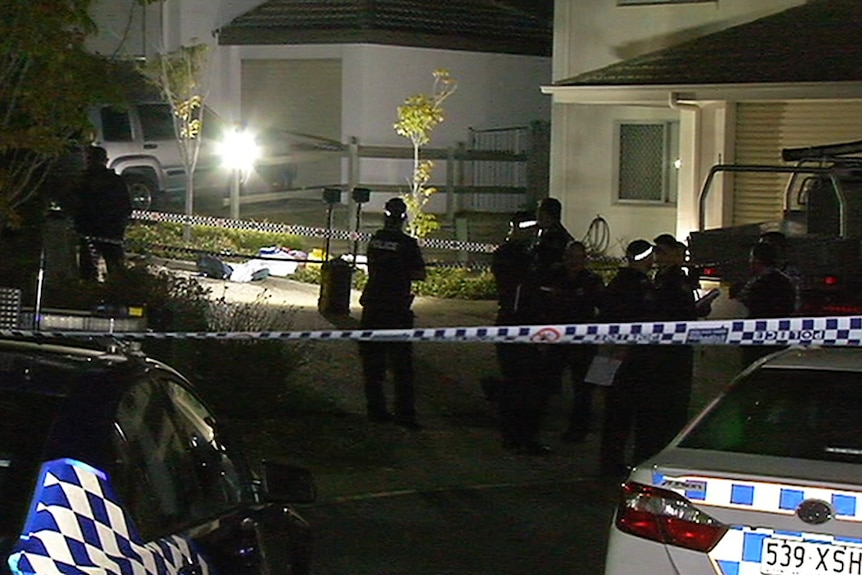 Police around a covered body lying in a garden bed outside a townhouse complex